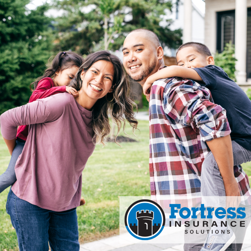 A mom and dad, smiling at the camera, each carrying one of their children on their back. 